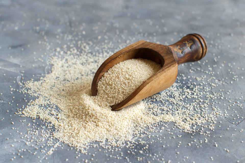 Raw uncooked fonio seeds with a spoon on grey background close up