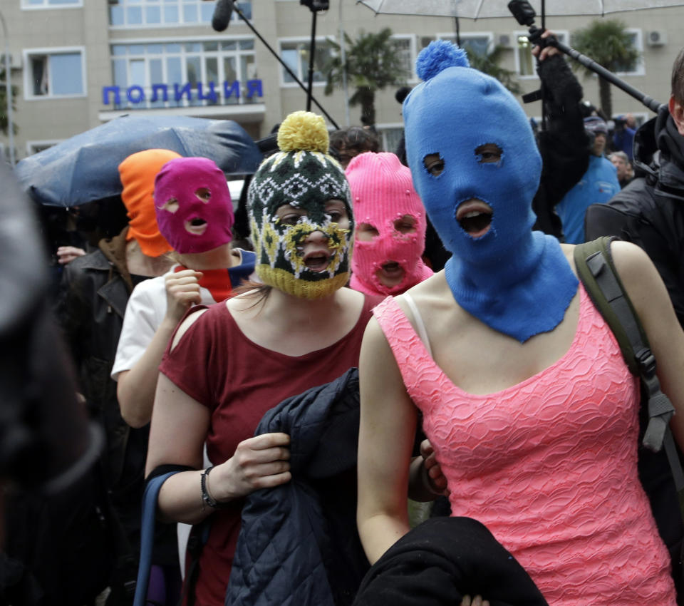 Five women wearing balaclavas, two of whom are members of the Russian punk group Pussy Riot, make their way through a crowd after they were released from a police station, Tuesday, Feb. 18, 2014, in Adler, Russia. No charges were filed against the Pussy Riot members Nadezhda Tolokonnikova, in the blue balaclava, and Maria Alekhina, in the pink, who were held along with several other people near the city's ferry terminal. (AP Photo/Morry Gash)