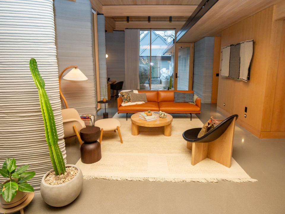 The living room inside the 3D printed home with lounge chairs, a rug, plants, and lights.