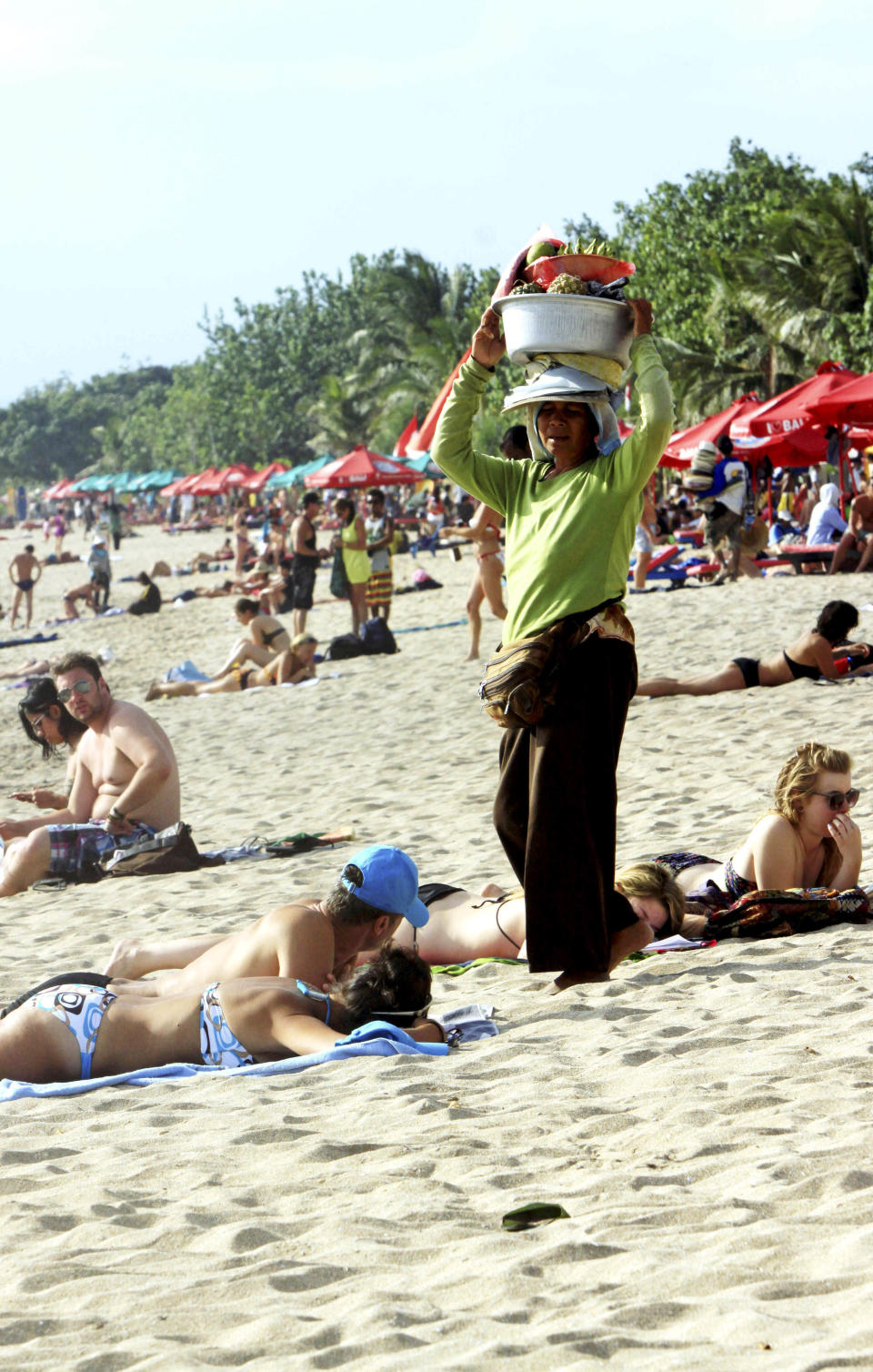 This Aug. 25, 2012 photo shows a Balinese vendor selling fruit to tourists on Kuta beach, Bali, Indonesia. Bali expects to find an undiscovered paradise. It can be hard to find Bali's serenity and beauty amid the villas with infinity pools and ads for Italian restaurants. But the rapidly developing island's simple pleasures still exist, in deserted beaches, simple meals of fried rice and coconut juice, and scenes of rural life. (AP Photo/Firdia Lisnawati)