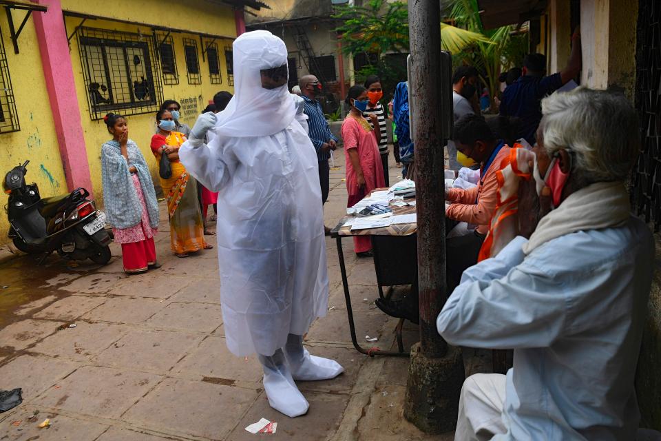 <p>A health worker wearing protective gear waits to collect swab samples from residents</p>AFP via Getty Images