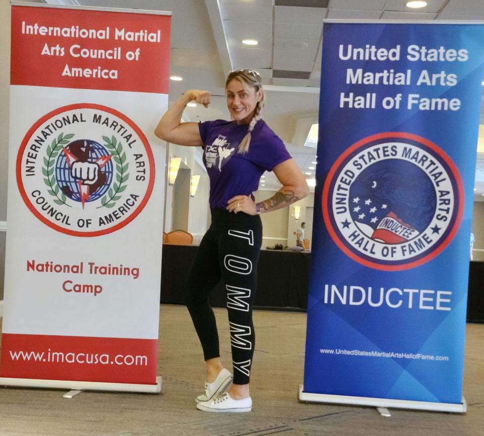 Shannon Hall-Girolamo flexes next to a couple of banners at the United States Martial Arts Hall of Fame induction ceremony in Houston in July.