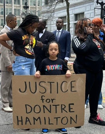 D.J. Jones holds a sign as he and other members of Dontre Hamilton's family prepare to march through downtown Milwaukee to mark the 10-year anniversary of Hamilton's fatal shooting by police. D.J.'s mother, Tasia Jones, is to his right.