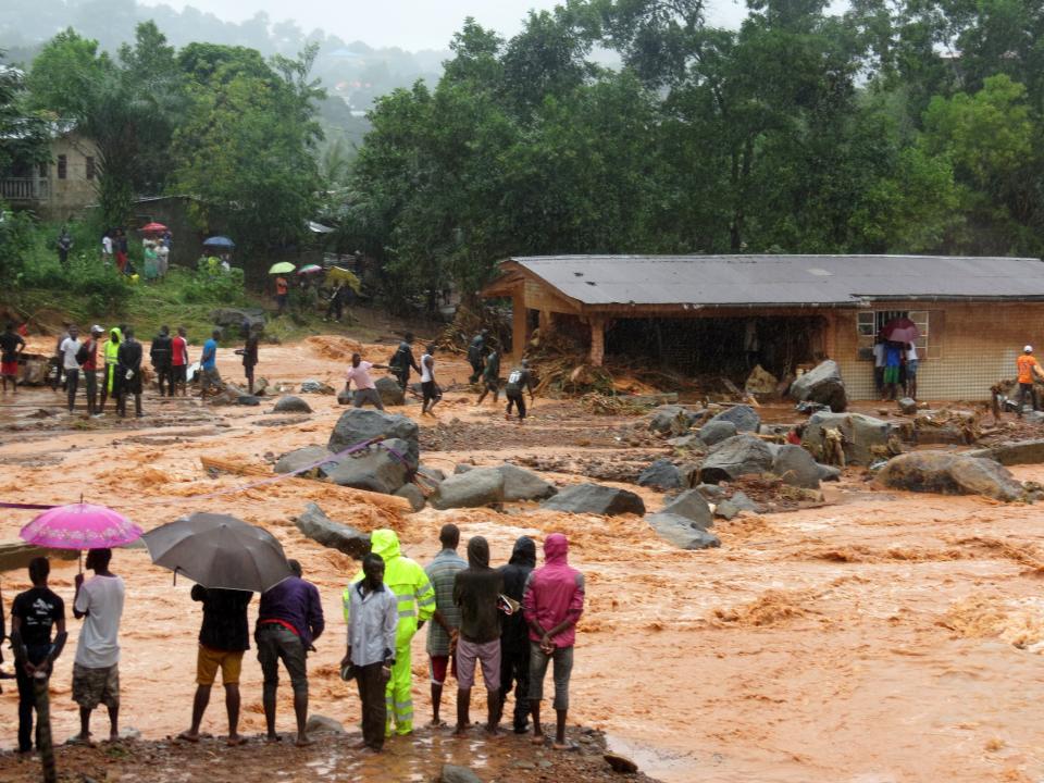 Bystanders look on as floodwaters rage past a damaged building in an area of Freetown on&nbsp;Aug. 14, 2017, after landslides struck the capital of the west African state of Sierra Leone.