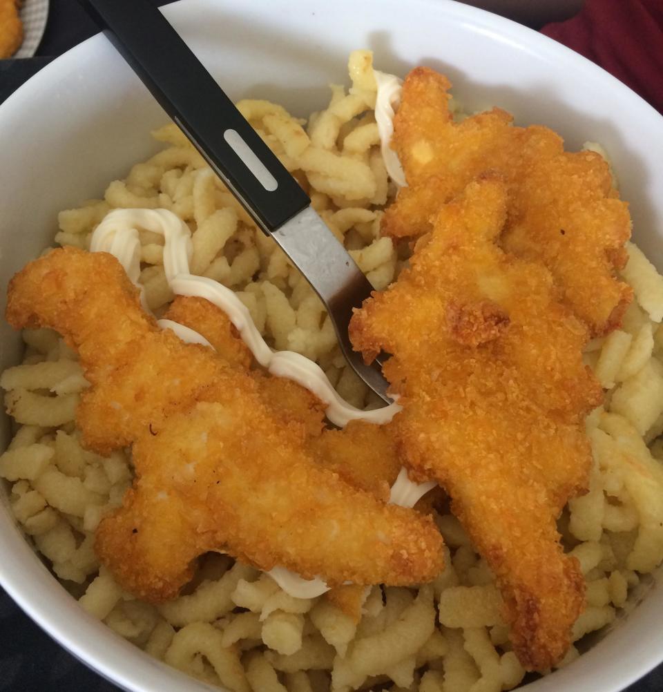 A bowl with noodles, 3 dino nuggets, and mayo drizzled on top