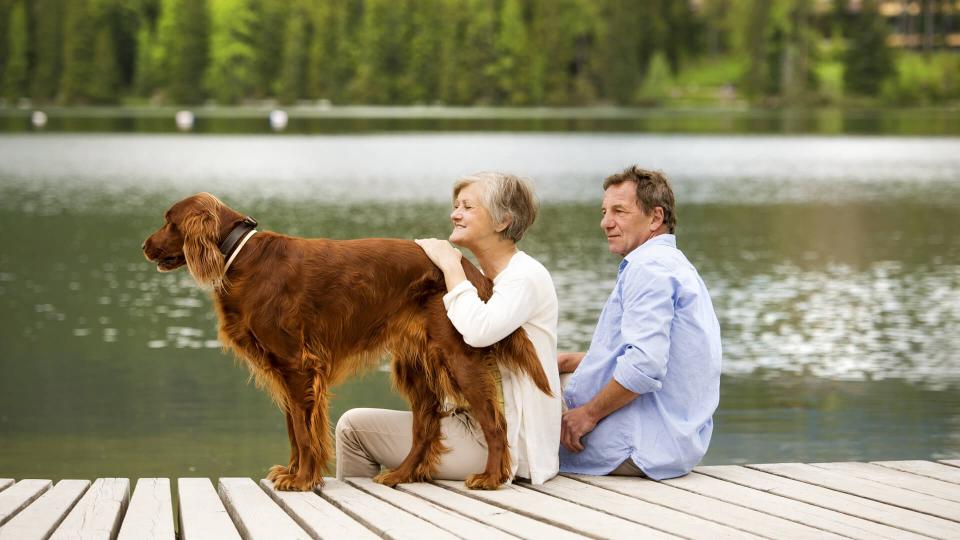 Senior couple with dog sitting on pier above the mountain lake with mountains in background.