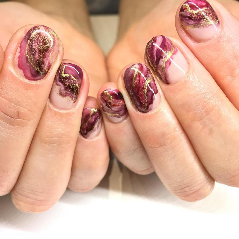 Negative-space manis aren't just a spring and summer look. With rich shades like mulberry mixed into a marble effect with warm, shimmering gold, <a href="https://www.instagram.com/p/BwXDXD5lG4j/" rel="nofollow noopener" target="_blank" data-ylk="slk:as Katie Masters did here;elm:context_link;itc:0;sec:content-canvas" class="link ">as Katie Masters did here</a>, leaving an asymmetrical hint of naked nails has never looked more autumnal.