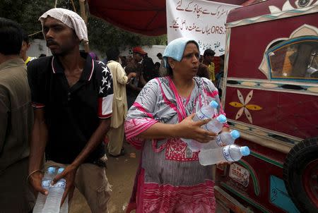 Volunteers cover their heads with water-soaked towels, to beat the heat, while distributing water bottles, outside Jinnah Postgraduate Medical Centre (JPMC) in Karachi, Pakistan, June 25, 2015. REUTERS/Akhtar Soomro