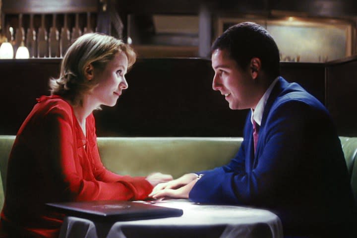 Emily Watson and Adam Sandler sit at a table together in Punch-Drunk Love.