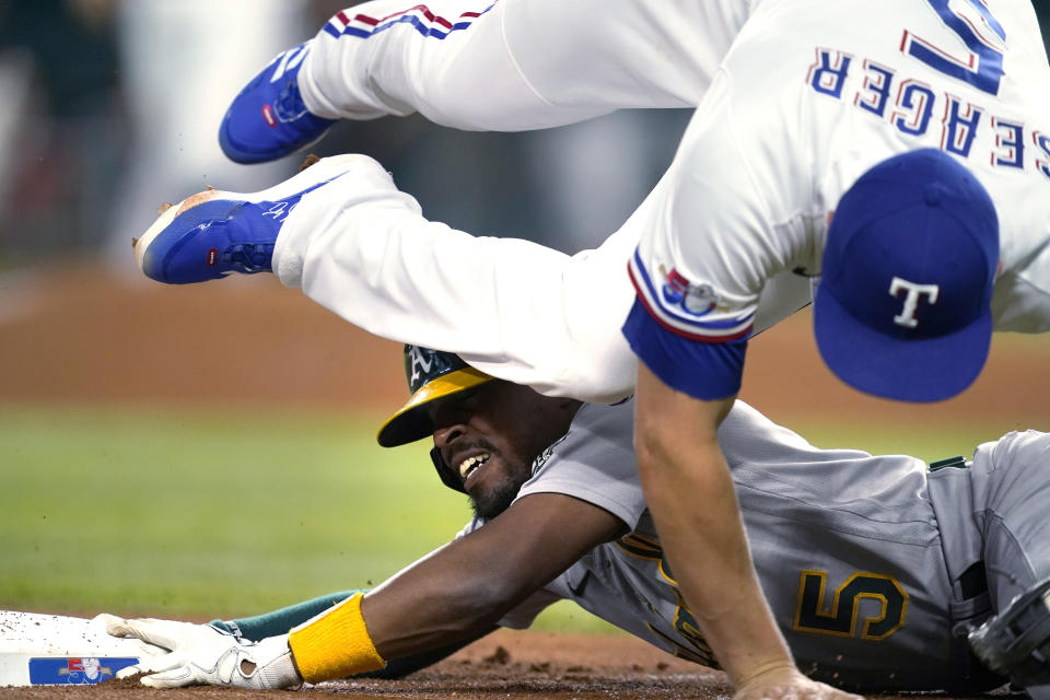 Oakland Athletics' Tony Kemp holds on to third base as Texas Rangers shortstop Corey Seager falls over him while grabbing the throw during the first inning of a baseball game in Arlington, Texas, Tuesday, Aug. 16, 2022. Kemp advanced to third on a single by Seth Brown that also scored Cal Stevenson. (AP Photo/Tony Gutierrez)