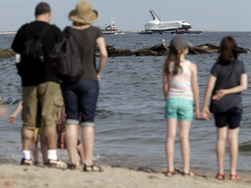 Spectators watch the space shuttle Enterprise as it is towed past a beach at Coney Island in New York, Sunday, June 3, 2012. The prototype space shuttle that arrived in New York City by air earlier this spring is on the move again, this time by sea, to it's final resting place at the Intrepid Sea, Air and Space Museum on the west side of Manhattan. (AP Photo/Seth Wenig)