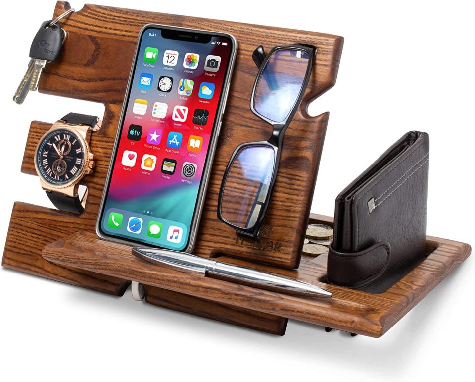 A wooden phone docking station including slots for keys, watch, glasses, wallet and pen on a white background