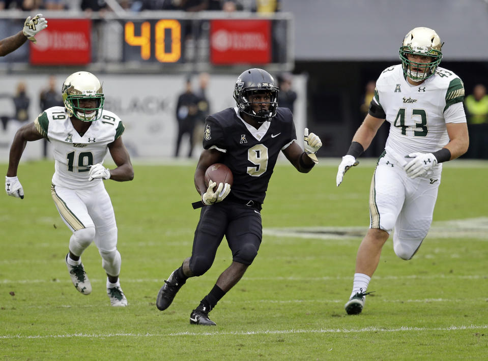 Central Florida running back Adrian Killins Jr. (9) runs for yardage between South Florida cornerback Ronnie Hoggins (19) and linebacker Auggie Sanchez (43) during the first half of an NCAA college football game, Friday, Nov. 24, 2017, in Orlando, Fla. (AP Photo/John Raoux)