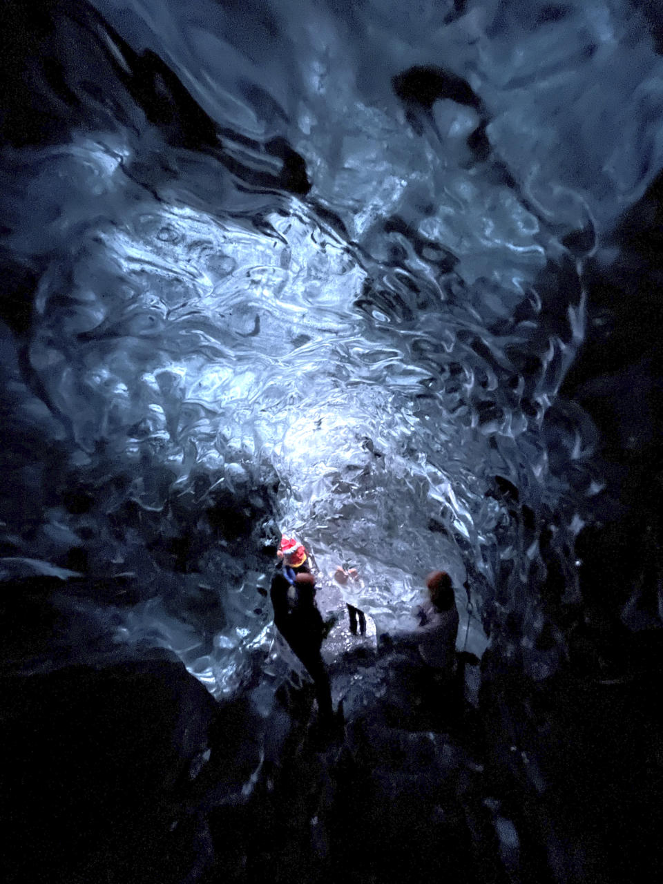 This Nov. 18, 2023 image provided by Beth Harpaz shows visitors in an ice cave at Vatnajokull National Park, located on an ice field in southeastern Iceland. The caves can only be explored on a tour with a registered guide. Winter crampons must be attached to shoes and boots for traction to avoid slipping. (Beth Harpaz via AP)