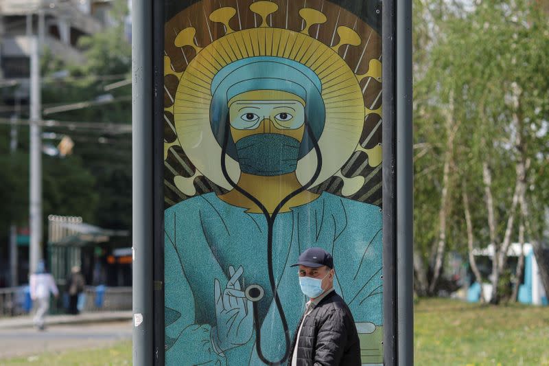 A man passes by an outdoor poster that shows a medic depicted in a similar manner as Jesus Christ would be portrayed by Christian Orthodox religious paintings