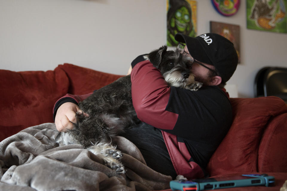 Eli cuddles his dog on the couch at his home in Casselberry, Fla., May 29, 2023. Eli and his fiancé Lucas, both transgender men, plan to move to Minnesota with their dog and two cats later this year. The Associated Press is not using Eli’s and Lucas’ last names because they fear reprisal. Minnesota is among the states this year that have codified protections for transgender people in response to sweeping anti-LGBTQ legislation in mostly Republican-led states. (AP Photo/Laura Bargfeld)