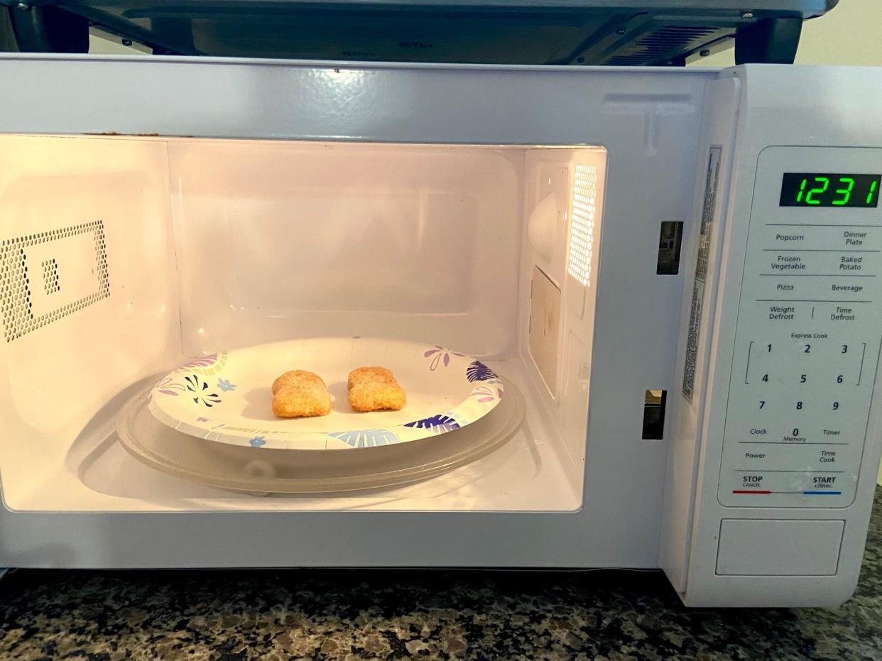 2 nuggets on a paper plate in an white microwave with the door open.