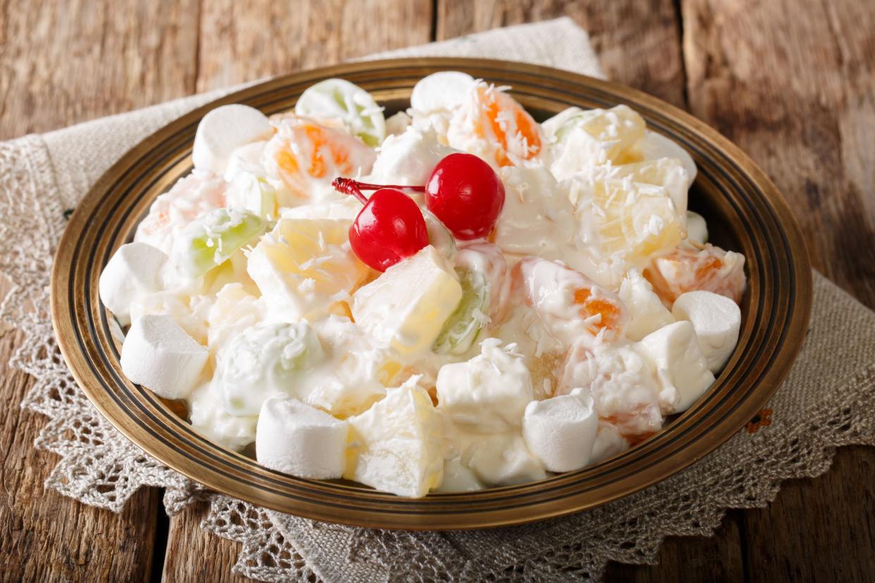 fruit salad from pineapple, oranges, grapes and coconut with marshmallow and vanilla yogurt close-up on a plate. horizontal