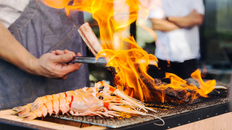 Person cooking food on a grill with flames