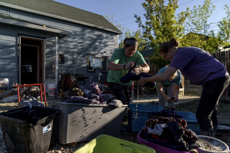 Kirstyn Brown, right, cleans out damaged clothing from her flooded home with the help of her mother, Cheryl Pruitt, rear, and her sister-in-law, Randi Pruitt, in Red Lodge, Mont., Wednesday, June 15, 2022. (AP Photo/David Goldman)