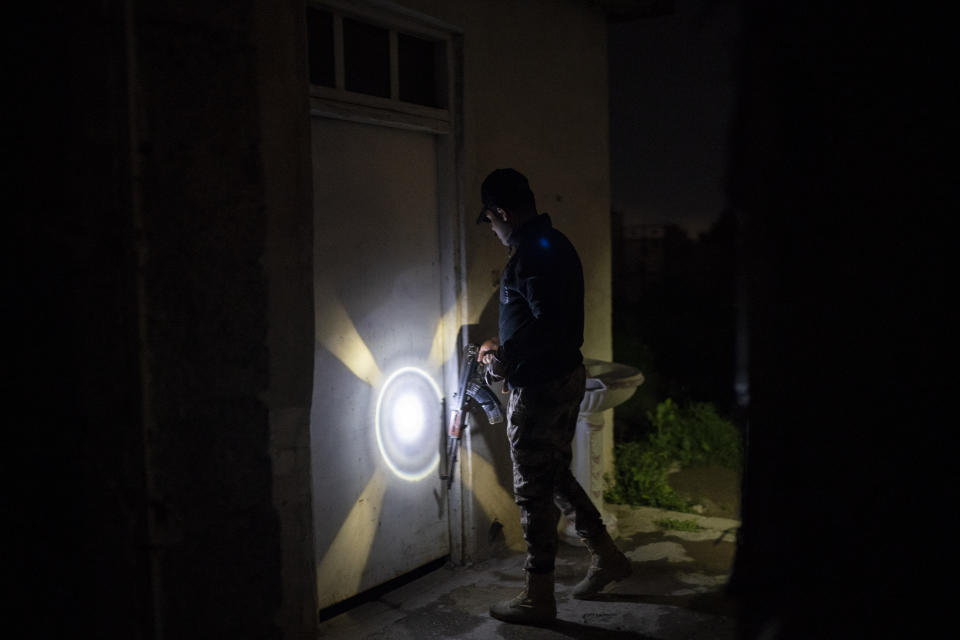 In this April 2, 2019 photo, an Iraqi army 20th division soldier uses his AK-47 rifle to knock on a door during a nighttime raid near Badoush, Iraq. A year and a half after the Islamic State group was declared defeated in Iraq, the northern Iraqi town is a key battleground between security forces trying to stamp out the group's remnants and the militants who have reverted to insurgency. (AP Photo/Felipe Dana)