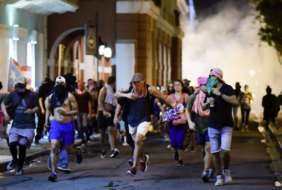 Demonstrators affected by tear gas thrown by the police run during clashes in San Juan, Puerto Rico, Monday, July 22, 2019. Protesters are demanding Rossello step down following the leak of an offensive, obscenity-laden online chat between him and his advisers that triggered the crisis. (AP Photo/Carlos Giusti)