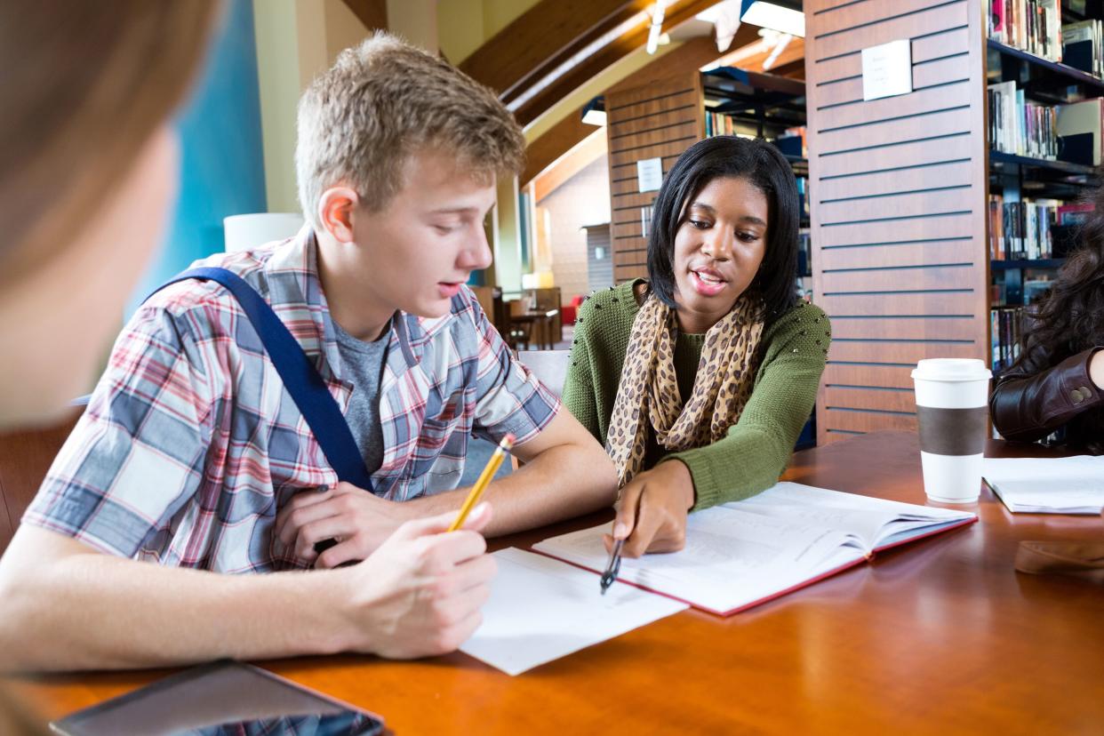college student tutoring high school boy in modern library