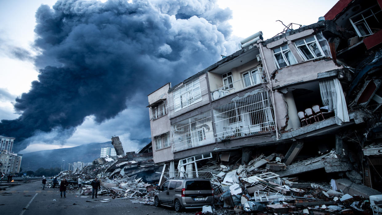  Smoke billows from a fire at the port as people inspect collapsed buildings in Iskenderun, Turkey.  