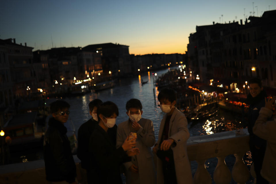 Tourists wearing protective masks pose for a photograph at the Rialto bridge as the sun sets in Venice, Italy, Friday, Feb. 28, 2020. Venice in the time of coronavirus is a shell of itself, with empty piazzas, shuttered basilicas and gondoliers idling their days away. The city has remained quiet ever since the outbreak, with only intrepid tourists wearing a different type of mask _ surgical _ remaining and taking advantage of a city that otherwise would be jammed. (AP Photo/Francisco Seco)