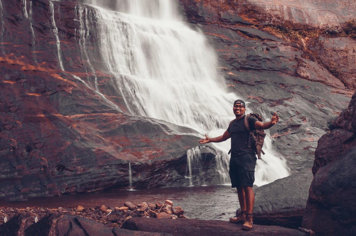 Black Man Standing In Front of A Waterfall