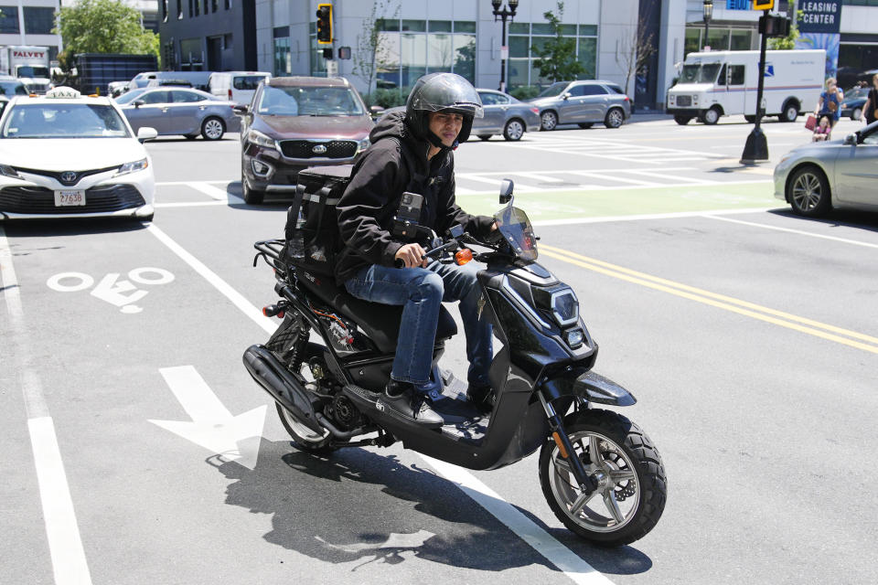 A delivery driver on a scooter heads out on a delivery in the Seaport District, Friday, June 7, 2024, in Boston. A soaring demand for food delivered fast has spawned small armies of couriers in a growing number of cities where delivery scooters, motorcycles and mopeds zip in and out of traffic and hop onto sidewalks alongside startled pedestrians racing to drop off salads and sandwiches. (AP Photo/Charles Krupa)