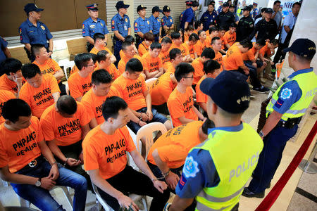 Policemen guard some of the 43 arrested foreigners, mostly Chinese nationals, for kidnapping a Singaporean woman at a casino resort in the capital, during a presentation inside the Philippine National Police (PNP) Headquarters in Quezon City, metro Manila, Philippines July 20, 2017. REUTERS/Romeo Ranoco