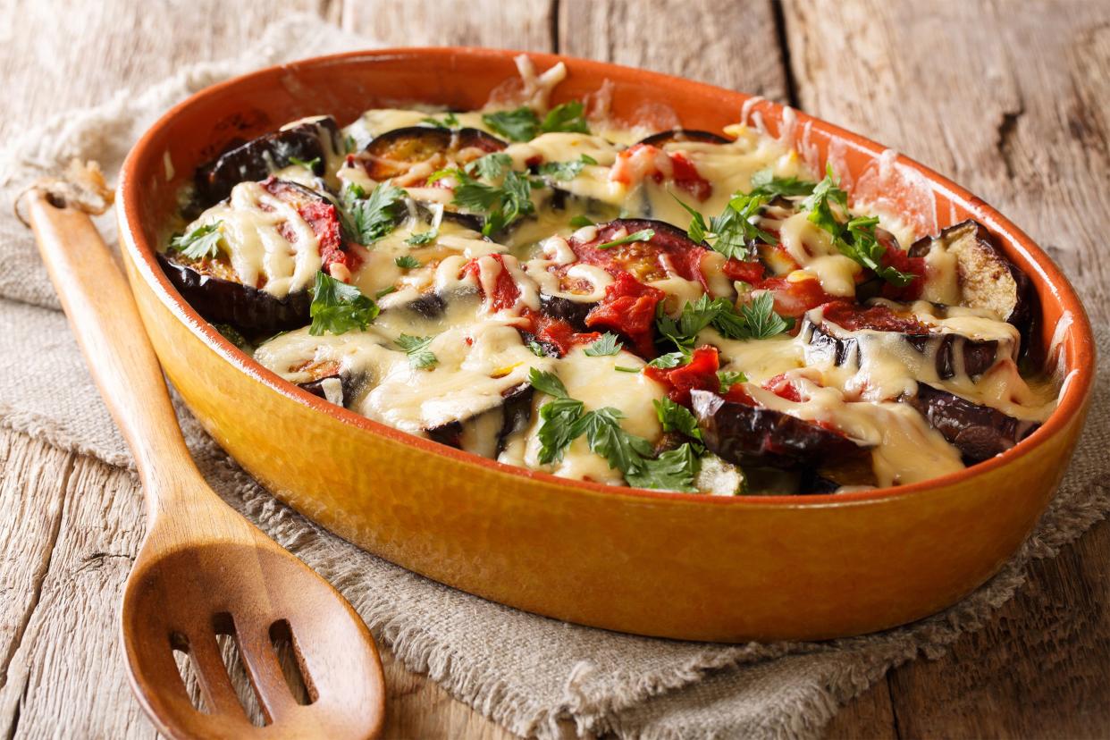 Eggplant Rollatini in an oval stone orange baking dish with a slotted wooden spoon