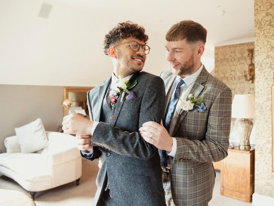 A groom hugs his groom from behind.