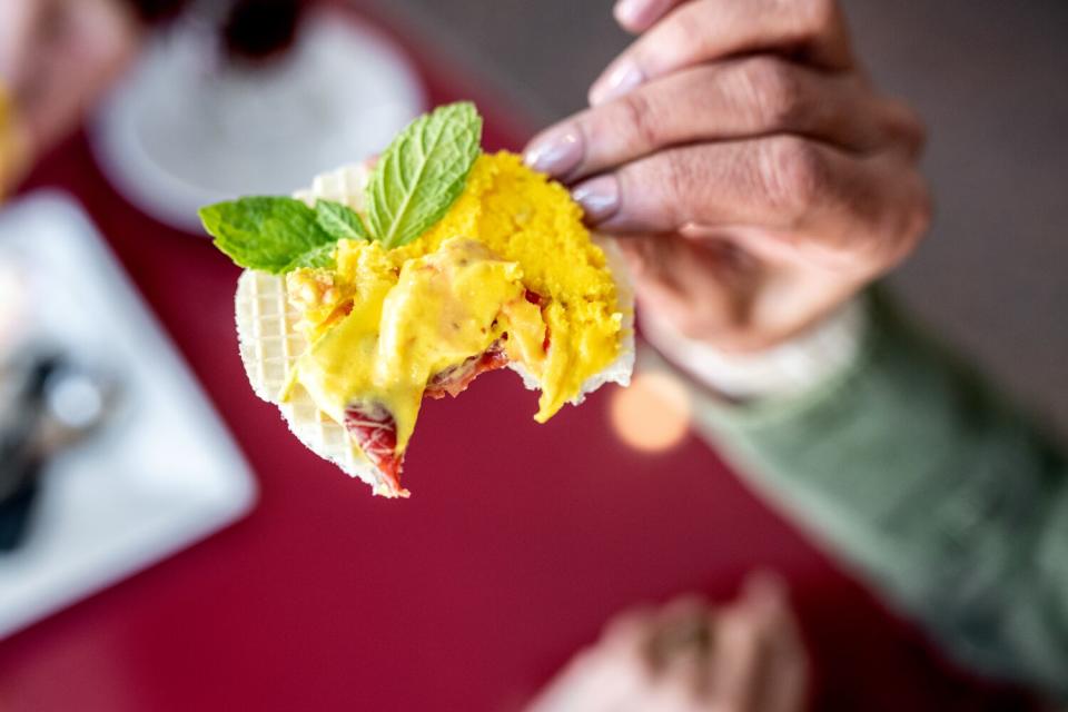 A woman's manicured hand holds a spoon of yellow ice cream