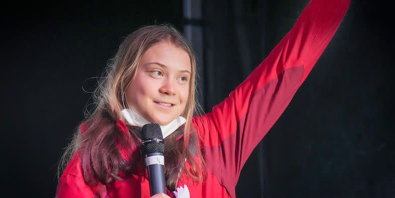 climate activist greta thunberg raises one fist and holds a microphone whilst on stage at a climate conference