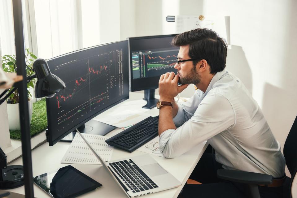 A person studying stock charts and graphs on multiple computer monitors.