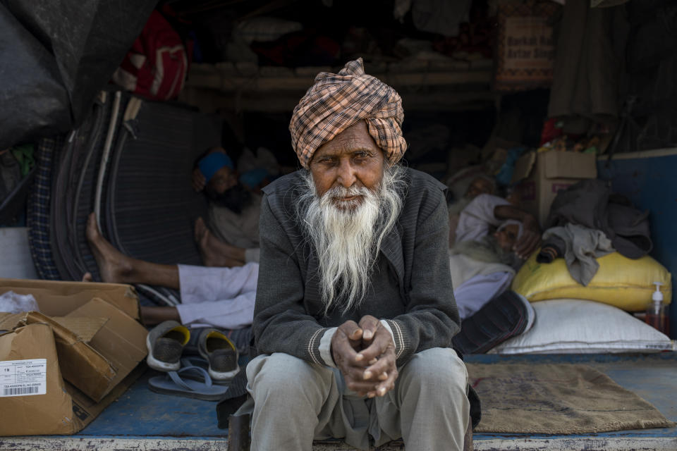 Amrik Singh Mikka, 78, sits for a photograph on the back of his tractor trailer parked on a highway during a protest against new farm bills at the Delhi-Haryana state border, India, Tuesday, Dec. 1, 2020. At night, the farmers sleep inside the trailers or under the trucks. During the day, they sit huddled in groups at the backs of the vehicles, surrounded by mounds of rice, lentils and vegetables. Every day, thousands more join the protesters. (AP Photo/Altaf Qadri)