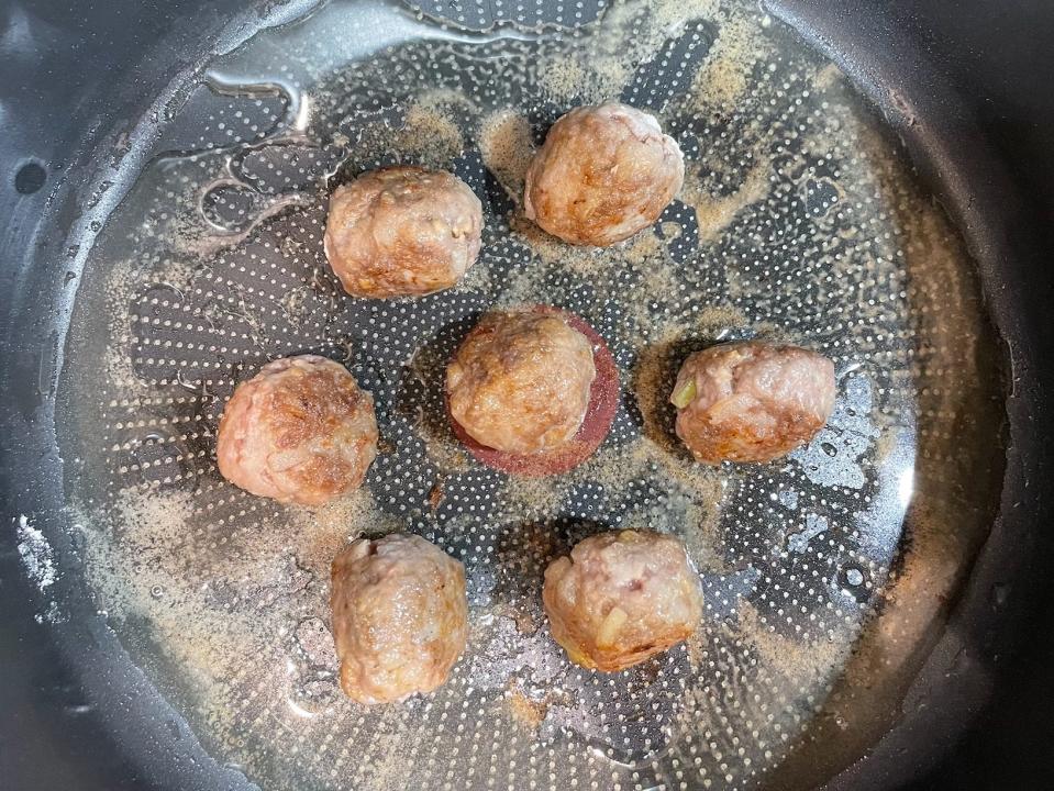7 homemade meatballs frying in oil in a pan