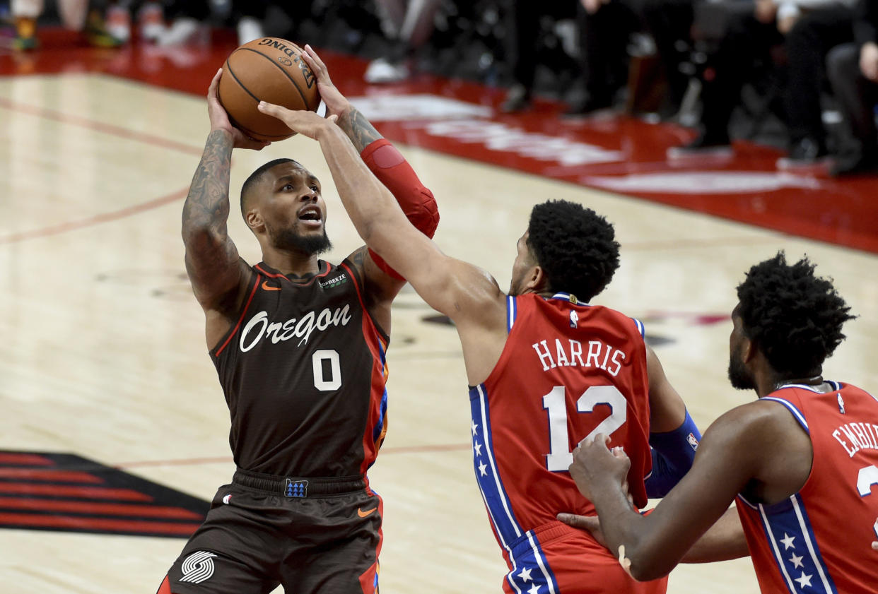 Damian Lillard with the ball in his hands to shoot over Tobias Harris with Joel Embiid coming in to help defend.