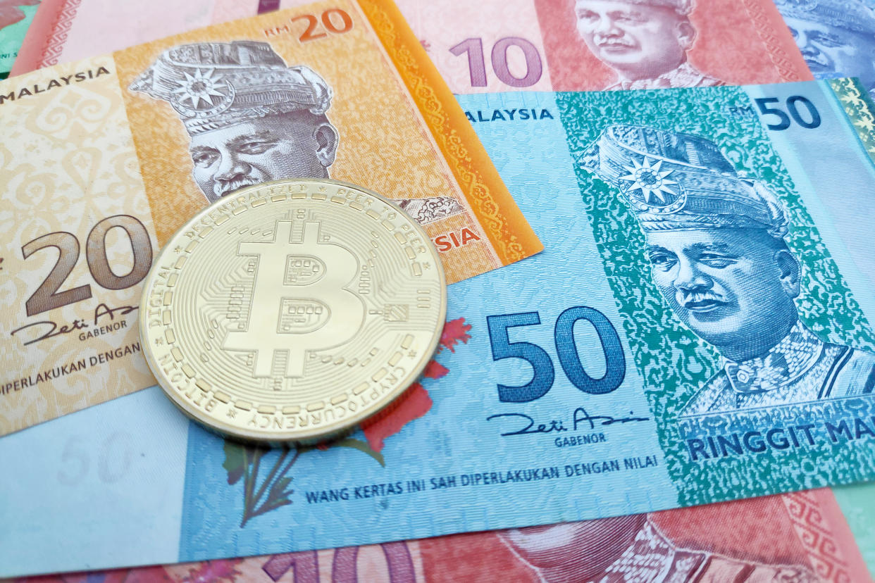 Close-up on a golden Bitcoin coin on top of a stack of Malaysian Ringgit banknotes.
