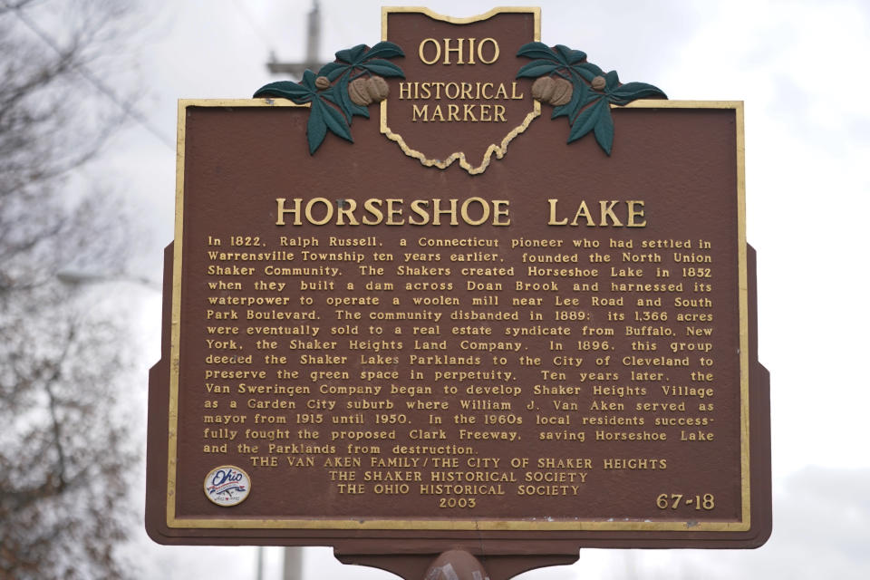 An Ohio historical marker sign stands near Horseshoe Lake, Tuesday, Dec. 7, 2021, in Cleveland Heights, Ohio. A pair of high-hazard dams built in the mid-1800s near Cleveland are among those in need of major repair. Upper Shaker Lake, commonly known as Horseshoe Lake, was drained as a precaution after it developed sinkholes and cracks. (AP Photo/Tony Dejak)