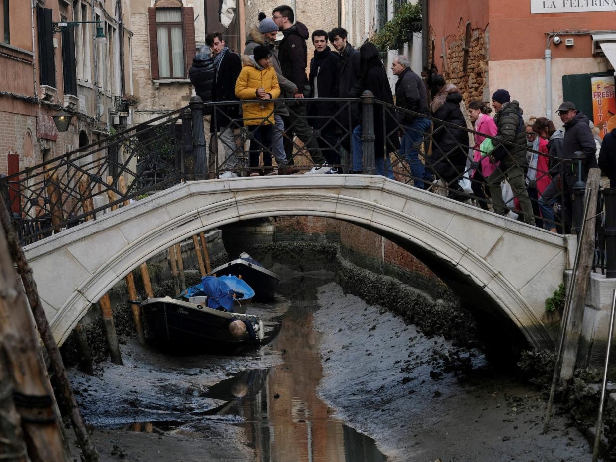 A crowd of tourists in Venice on February 17, 2023, on a bridge looking down at nearly-dry canal.