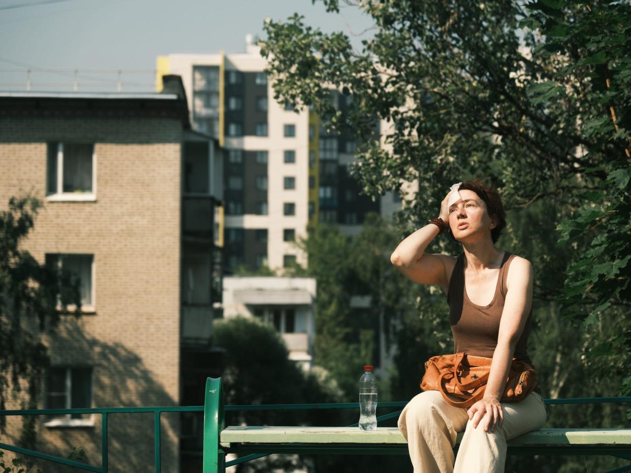 A woman sits on a bench and mops her brow in the summer heat