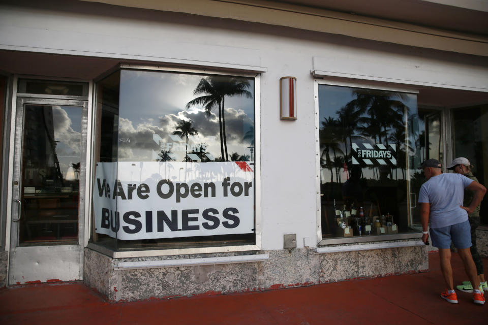 FILE - People peek into a window of a TGI Friday's restaurant to see what they are serving to-go on Wednesday, March 25, 2020, in Miami Beach, Fla. Some big corporate names are on the government’s list of 650,000 recipients of coronavirus relief loans despite the controversy that prompted other high-profile businesses to return billions of dollars in loan. TGI Friday's said the forced shutdowns left it with no more than 20% of its revenue, and that the loans allowed it to rehire furloughed staffers. (AP Photo/Brynn Anderson, file)