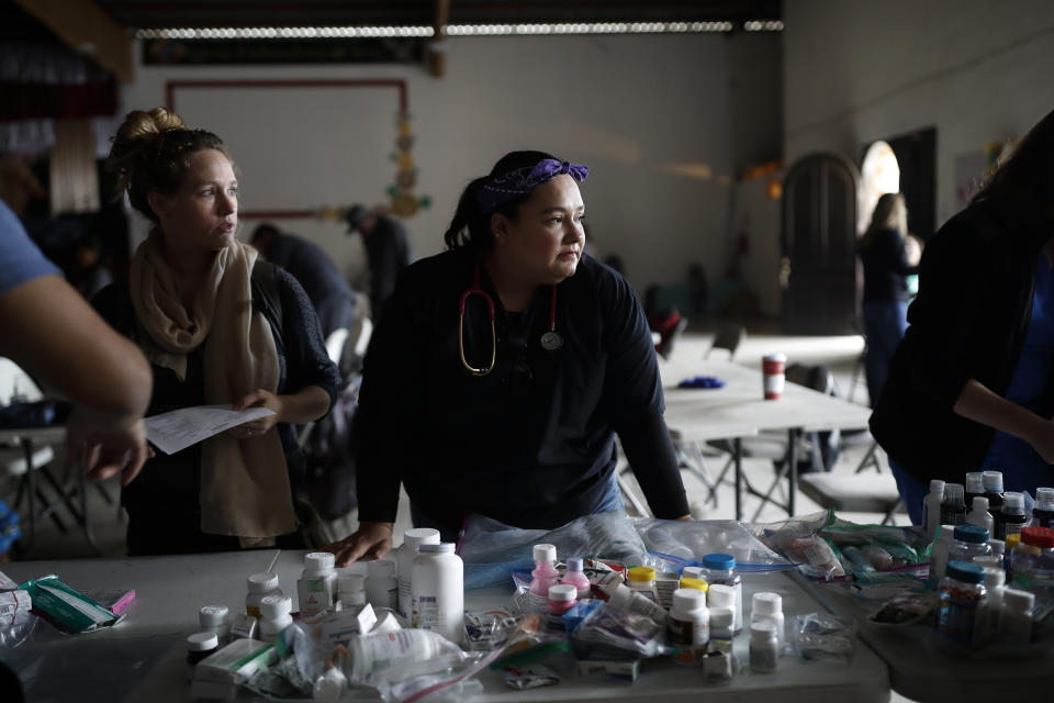In this Dec. 14, 2019, photo, Psyche Calderon, center, pauses for a moment as she works alongside other volunteer health care professionals in a shelter for migrants in Tijuana, Mexico. A burgeoning grassroots movement of health professionals and medical students from both sides of the U.S.-Mexico border is quietly battling on the front lines to keep asylum seekers healthy and safe. It is a daunting task taken on by volunteers trying to desperately tend to a need left largely unmet by the governments of both countries. (AP Photo/Gregory Bull)