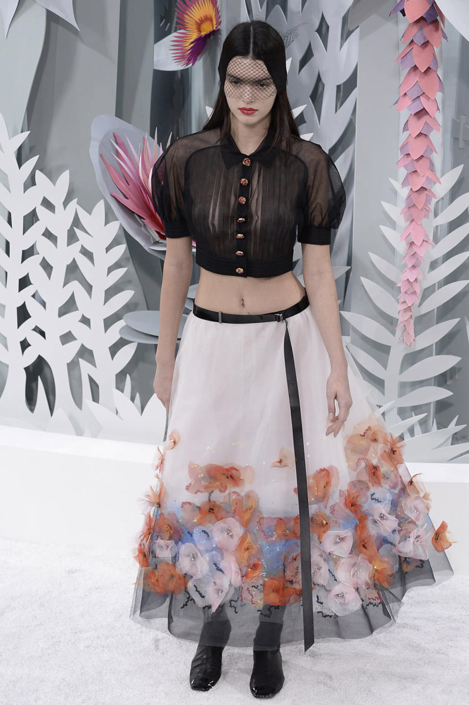 La nouvelle star des podiums Kendall Jenner a défilé pour Chanel en février 2015. Les matières vaporeuses apportent beaucoup de grâce à la jeune fille. L’opposition entre le noir et le blanc est adoucie par les fleurs cousues sur le bas de la robe. 