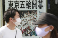 People wearing face masks to protect against the spread of the coronavirus walk past an extra paper reporting Tokyo Olympics start in Tokyo Saturday, July 24, 2021. (AP Photo/Koji Sasahara)