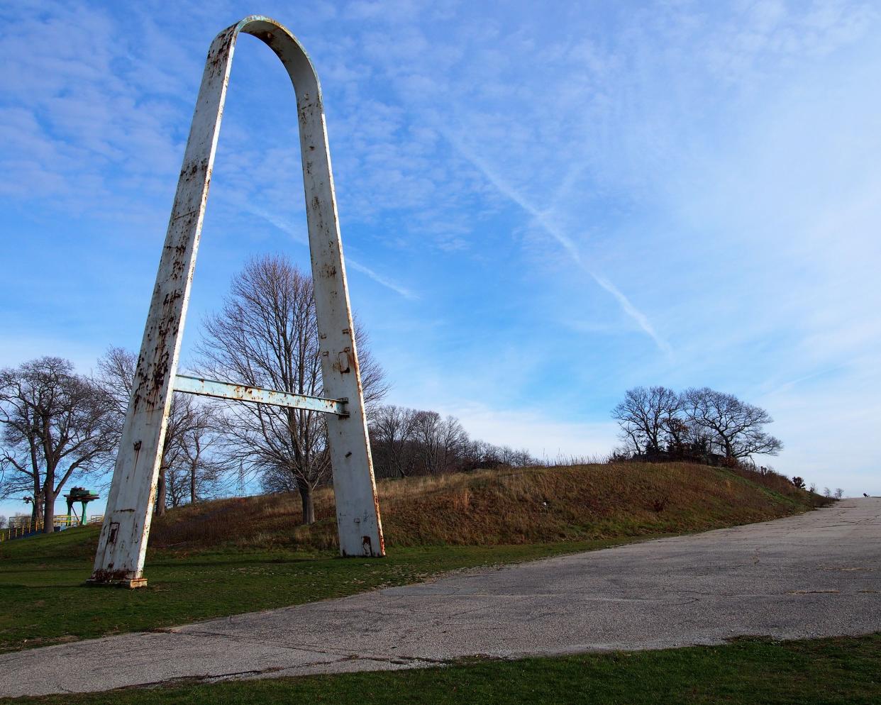 Abandoned Rocky Point Park, Warwick, Rhode Island, a rusted white arch on the left foreground with a sidewalk going up a hill on the right, bare trees and a dramatic blue sky, in winter