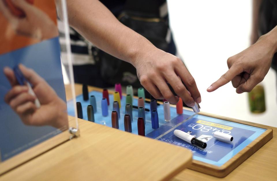 Visitors look at a pen-like "heat-not-burn" device at an IQOS store in Tokyo.